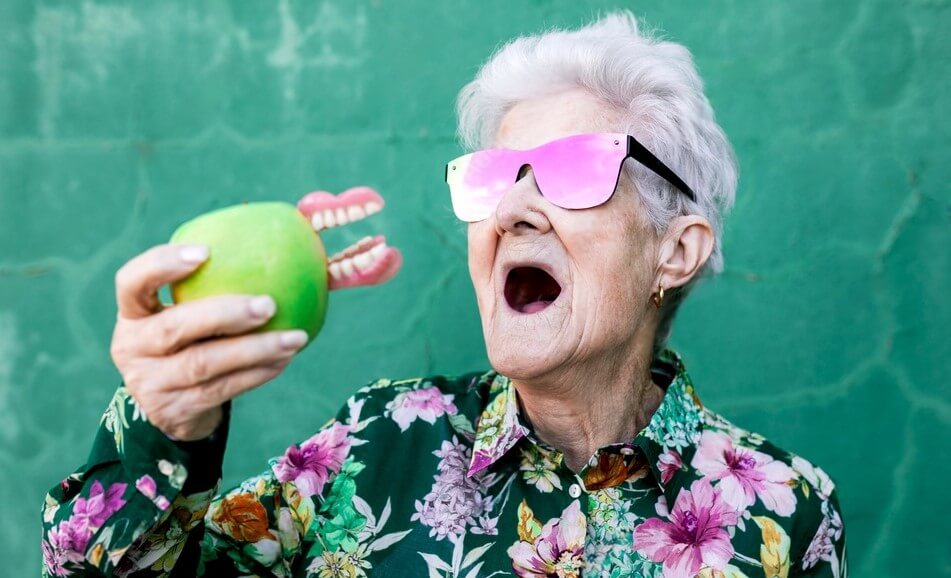 Old woman wearing shades leaves the dentures in the green apple