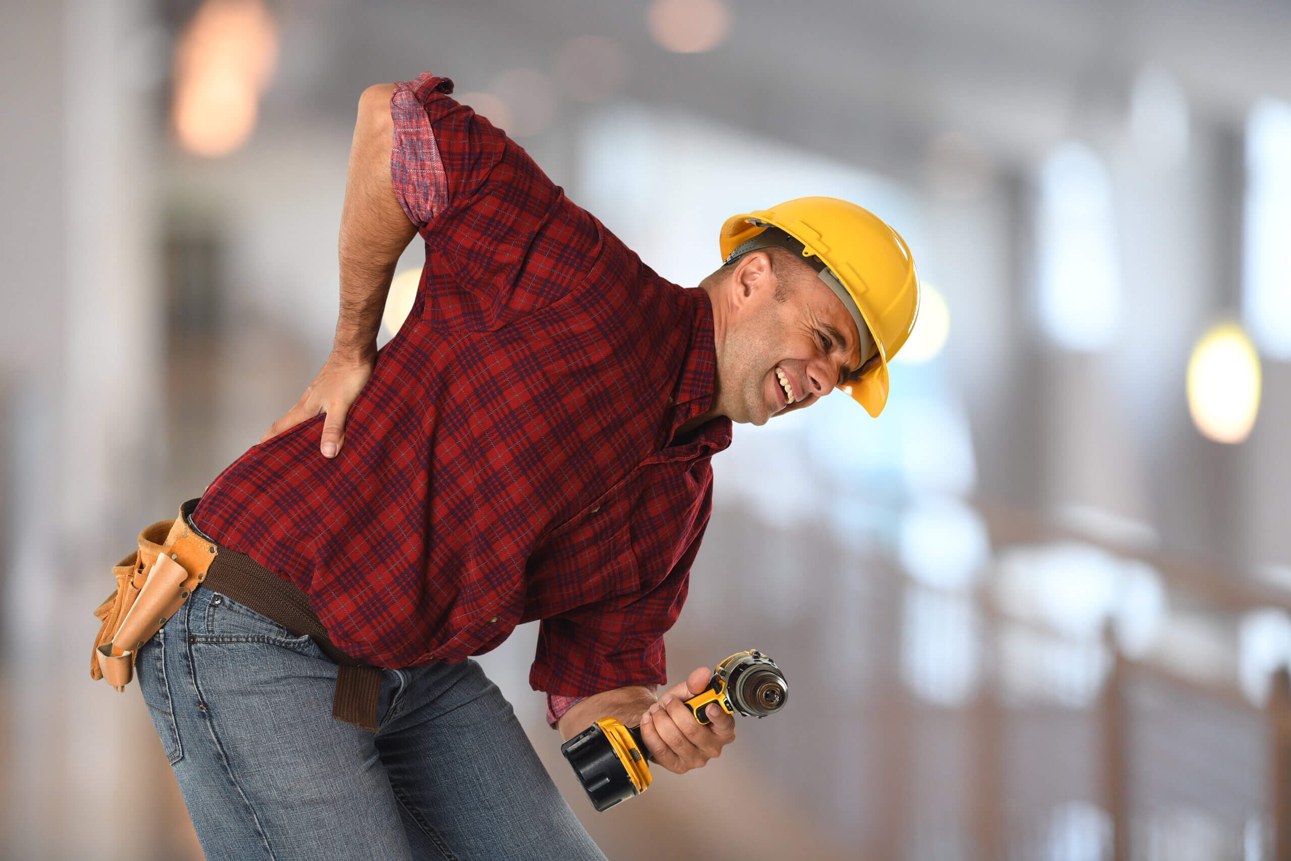 Worker experiencing sharp back pain while holding drill inside building